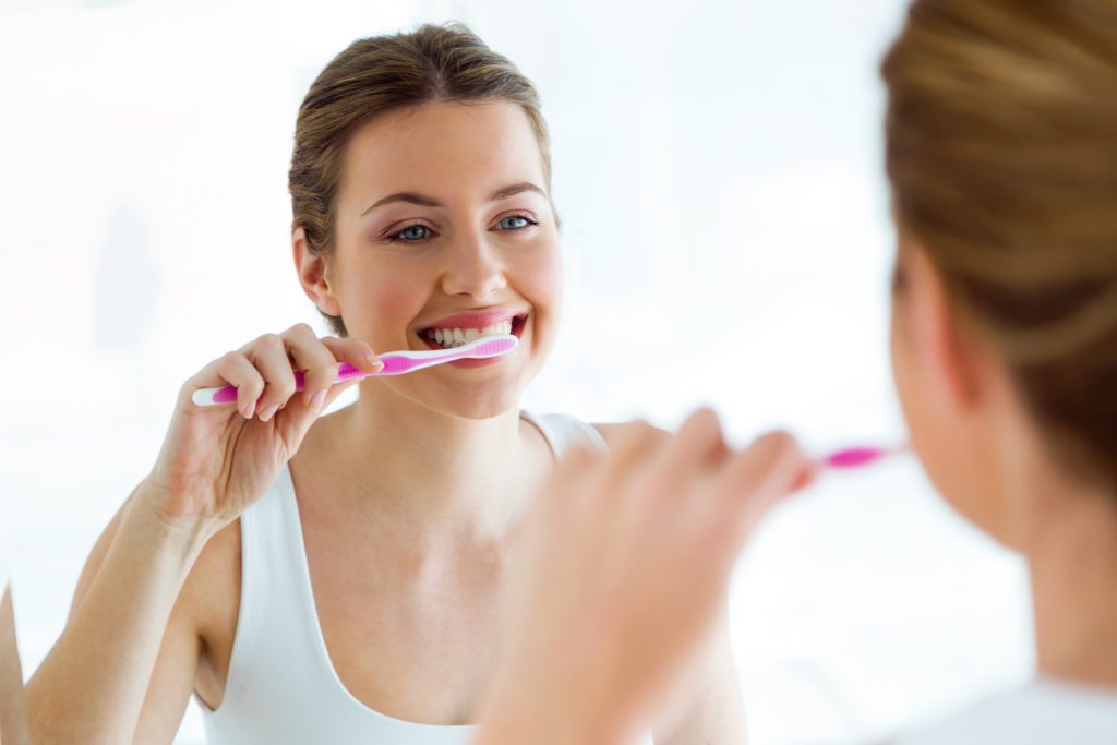 Woman brushing her teeth in the mirror oral hygiene dentist in Plano Texas