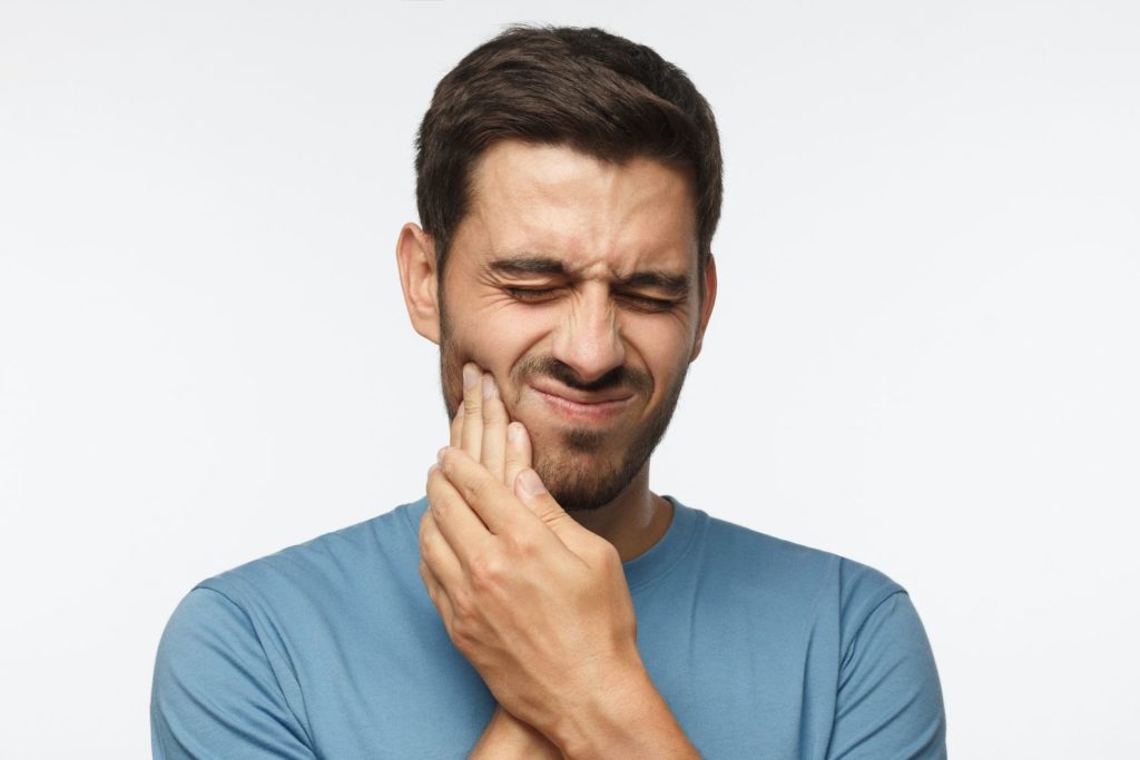 Young man holding his jaw with both hands indicating pain teeth grinding dentist in Plano Texas