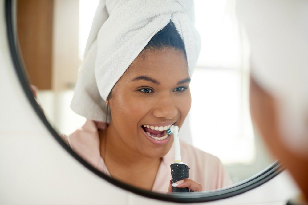 woman brushing her teeth in the mirror preventative dentistry dentist in Plano Texas